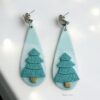Minimalist Christmas Tree Earrings handmade from polymer clay, featuring teal trees on a marbled background with stainless steel hooks.