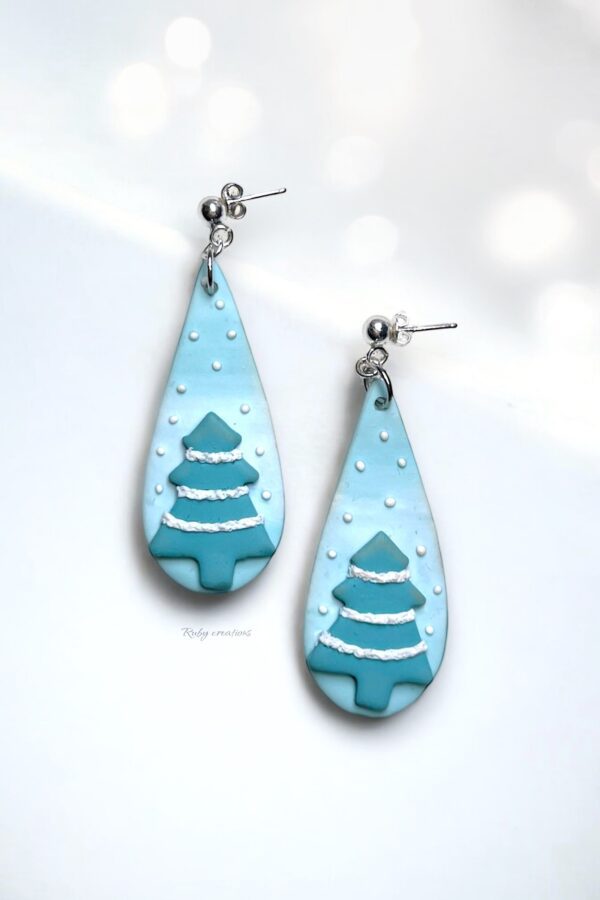 Snowy Christmas Tree Earrings handmade from polymer clay, featuring teal trees with white snow details on a soft blue background.